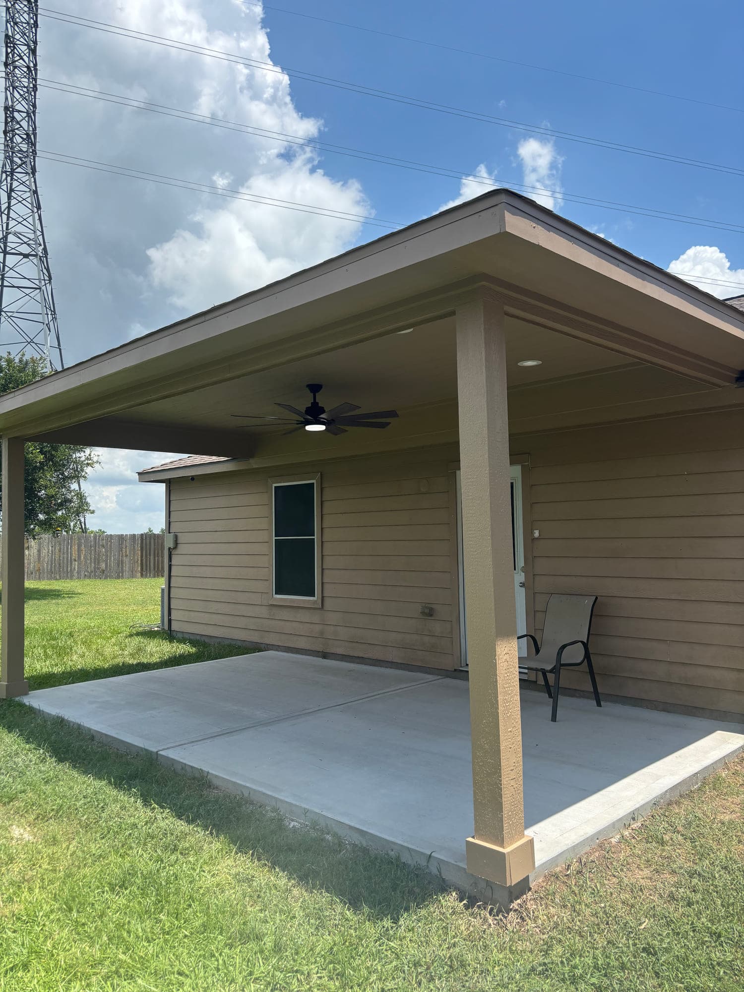 Attached hip-roof patio cover with a ceiling fan and boxed columns over a new concrete slab.