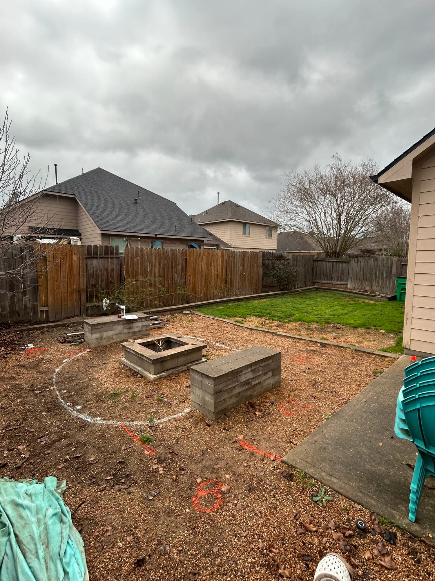 Bare backyard with exposed dirt, layout paint lines, and a partially built block fire pit before construction.