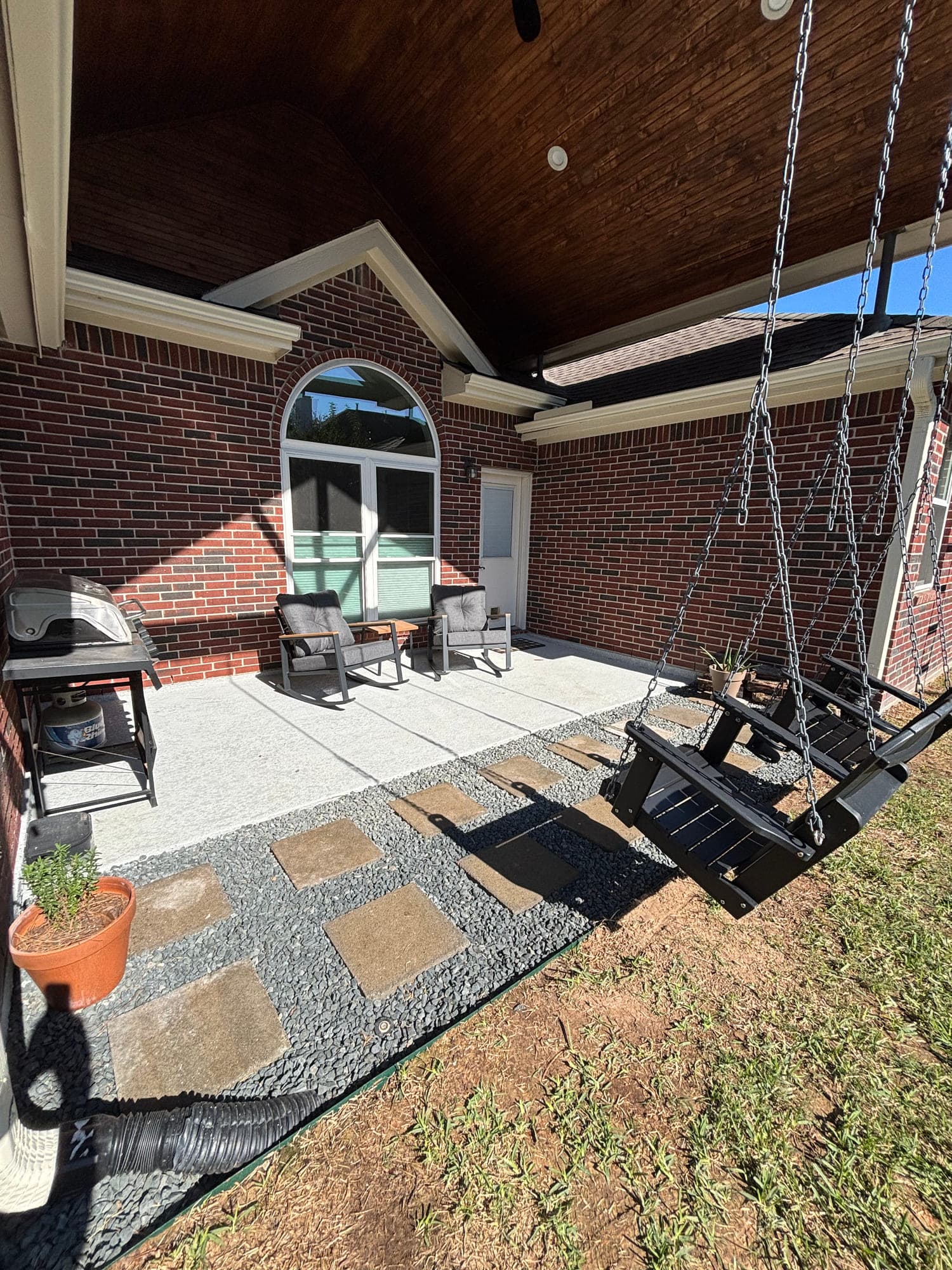 Cut flagstone stepping stones set in black gravel bordering a concrete patio under a covered porch.