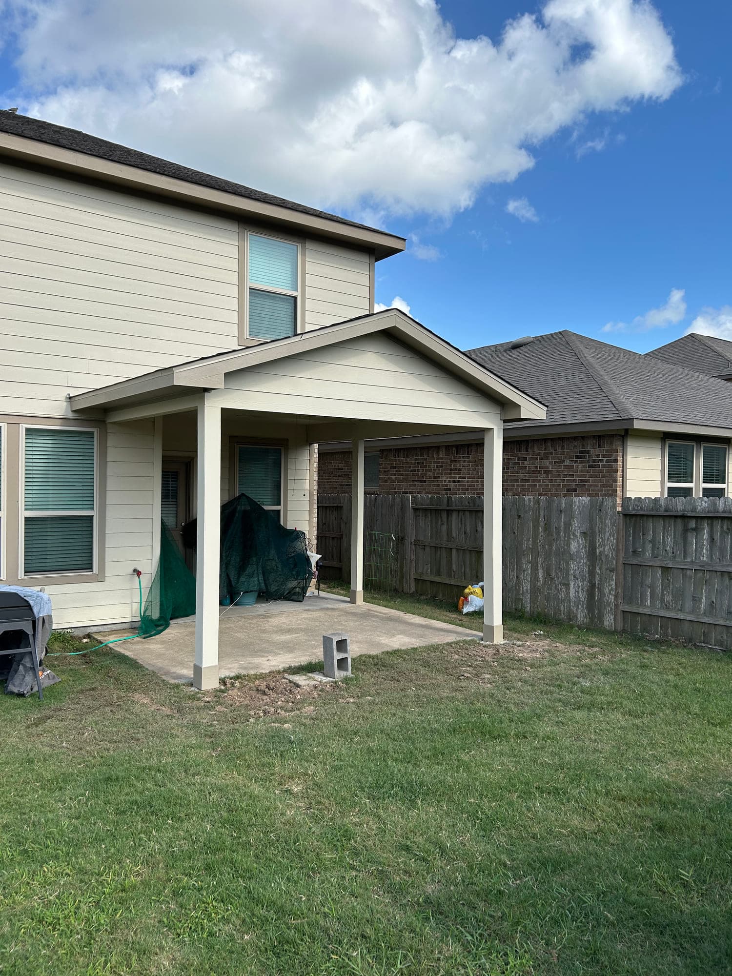 New gable patio cover framed and sided to match a two-story home, sheltering a poured concrete patio.