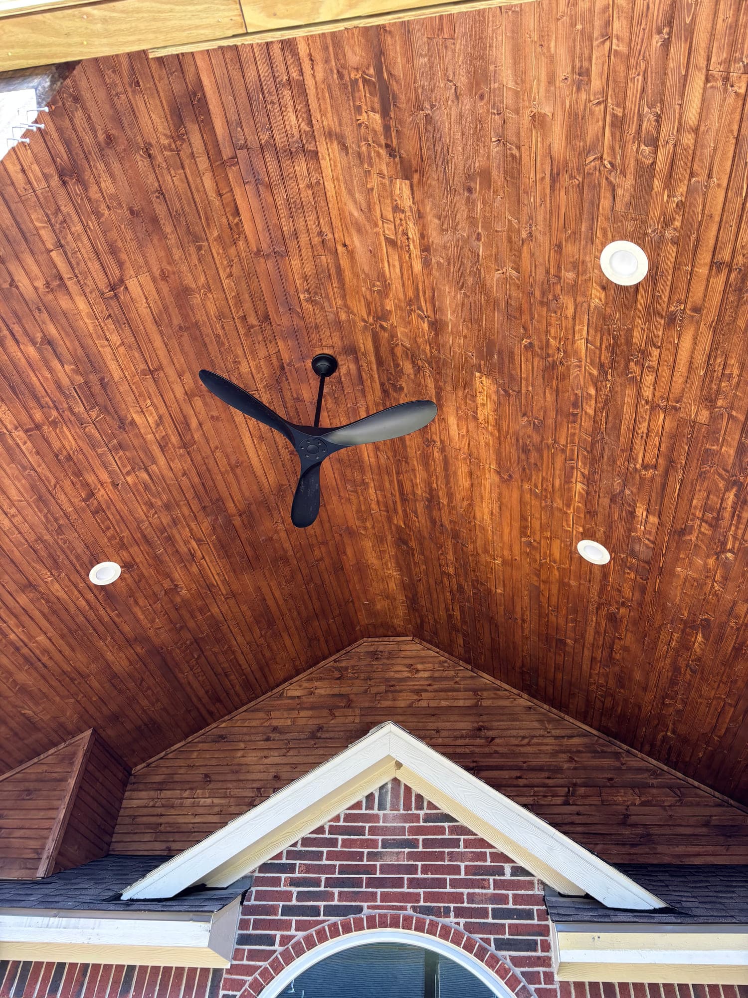 Vaulted tongue-and-groove wood ceiling with a matte black fan and recessed can lights inside a covered patio.