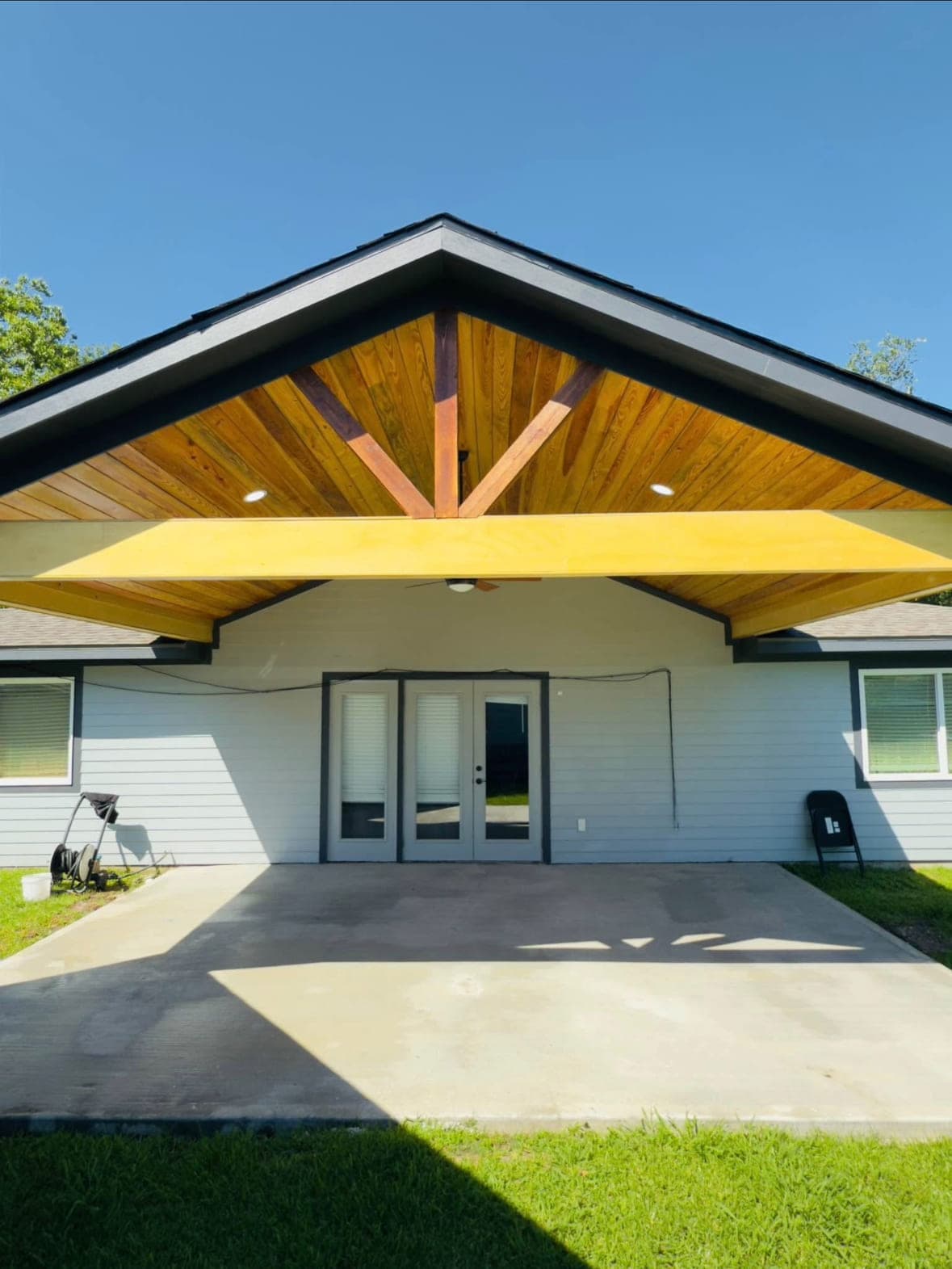 Vaulted patio cover with a warm cedar ceiling and exposed king-post truss above a broom-finished concrete patio.