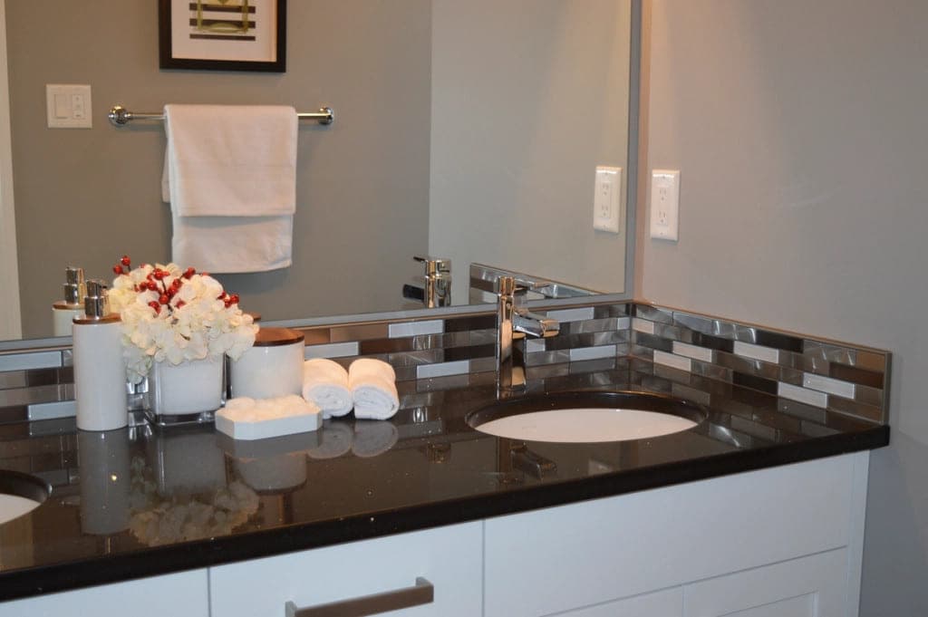 A bathroom vanity with a granite top, undermount basin and glass mosaic backsplash.